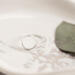 Single open circle sterling silver ring on white marbled dish with green leaf.

